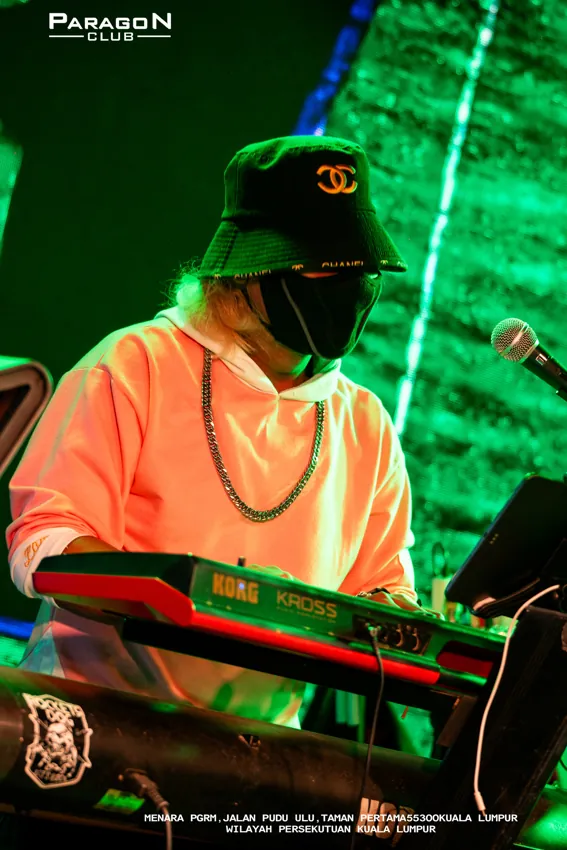 Keyboard player wearing a cap beneath green stage lighting at Paragon Club, Cheras